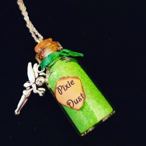 May include: A green glitter filled glass bottle with a cork stopper and a silver fairy charm. The bottle has a label that reads "Pixie Dust".