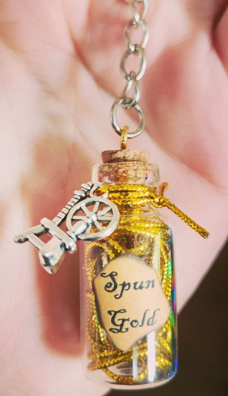 May include: A small glass bottle with a cork top filled with gold glitter and a small spinning wheel charm. The bottle has a label that says "Spun Gold".