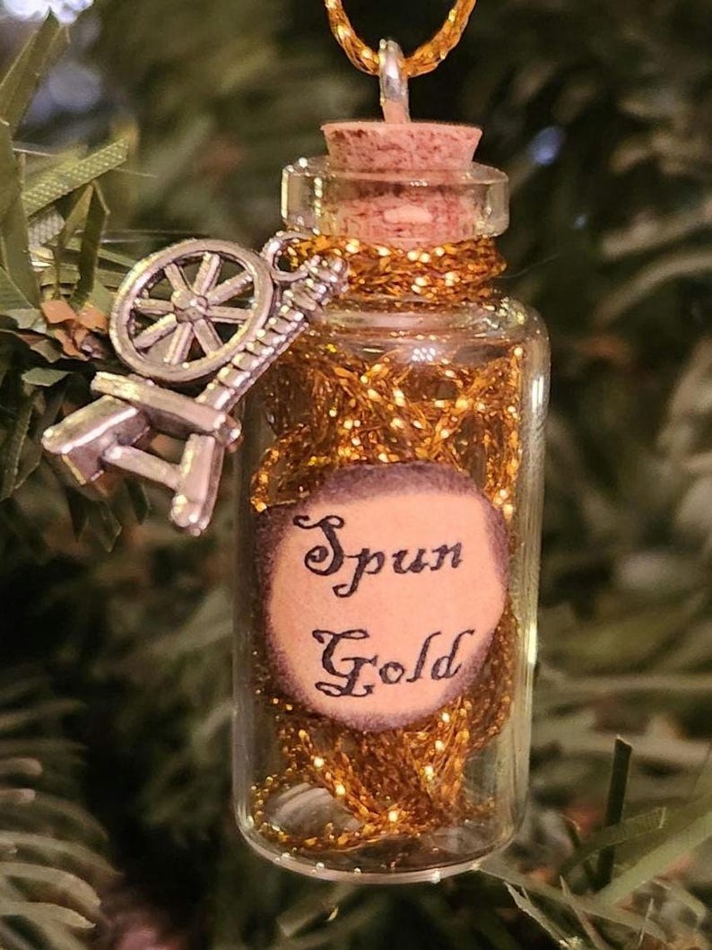 May include: A small glass bottle with a cork stopper filled with gold glitter and a spinning wheel charm. The bottle has a label that reads "Spun Gold".