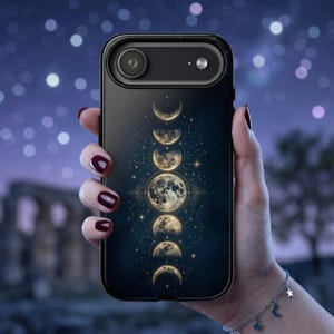 May include: Black phone case featuring a celestial design with phases of the moon in gold against a dark blue background. The case has a camera cutout and is held by a person with a silver bracelet.
