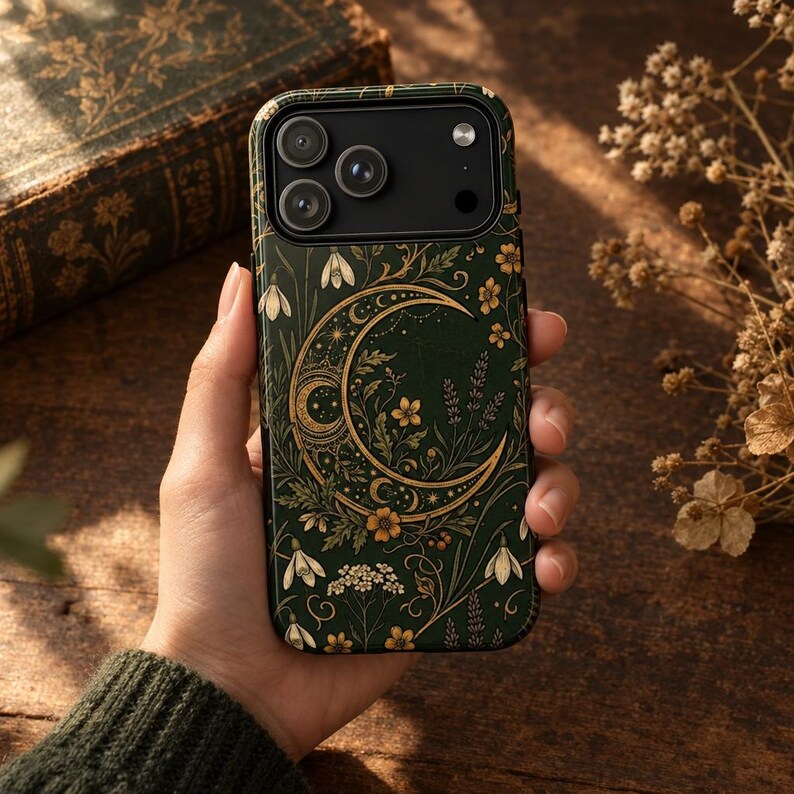 K&ouml;nnte beinhalten: Eine dunkelgr&uuml;ne Smartphone-H&uuml;lle mit einer goldenen Mondsichel-Illustration, umgeben von komplizierten botanischen Mustern, darunter kleine wei&szlig;e Bl&uuml;ten, gelbe Blumen und bl&auml;ttrige Ranken, mit einem schwarzen Ausschnitt f&uuml;r die Kameralinse.