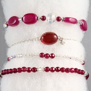 May include: Four bracelets with a variety of red beads and crystals. The top bracelet has large, oval-shaped beads. The second bracelet features a large, oval red stone. The third bracelet has small, round red beads. The bottom bracelet has small, faceted red beads.