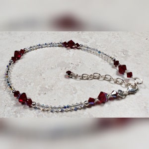 May include: A delicate silver anklet with a chain closure. The anklet is adorned with small, clear crystals and larger, red crystals.