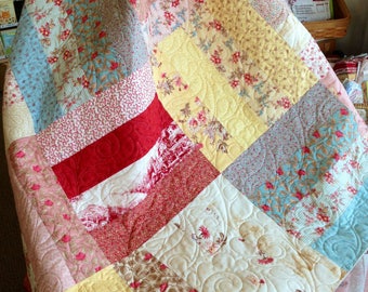 May include: A patchwork quilt featuring a range of floral patterns in shades of pink, red, yellow, and blue. The quilt is quilted with a swirling design.