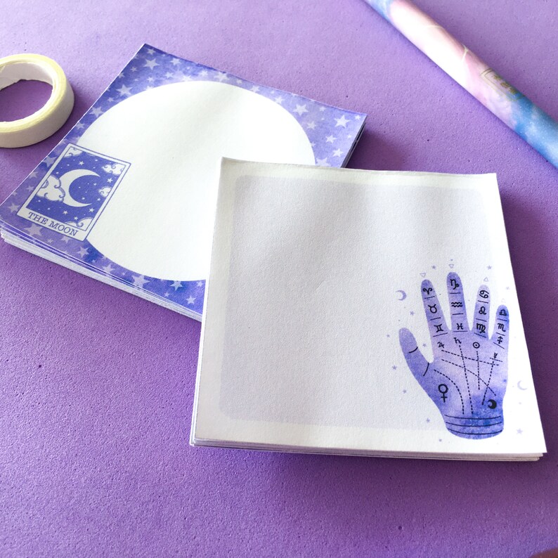 May include: A stack of purple and white notepads with a moon and stars design. The top notepad features a hand with astrological symbols and lines.