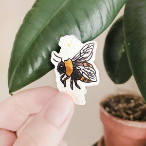 May include: A yellow and black bumblebee sticker with gold glitter accents. The sticker is on a white background.