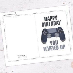 May include: A white greeting card with a dashed cut line and the text "cut me here". The card features a gray game controller graphic and the phrases "HAPPY BIRTHDAY" and "YOU LEVELED UP" in gray text.