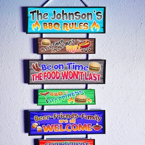 Puede incluir: Un letrero de pared colgante compuesto por seis placas rectangulares de madera conectadas por una cuerda blanca. Los letreros presentan gráficos coloridos de hamburguesas, salchichas y llamas con texto que incluye The Johnson's BBQ Rules, Never Touch Another Man's Grill, Be on Time The Food Won't Last, BBQ is Happiness, Beer-Friends-Family are all WELCOME y Compliment the COOK.