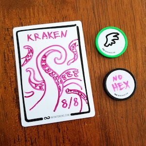 May include: A white card with a black border featuring a pink kraken illustration and the word "KRAKEN". Two circular tokens with the text "NO HEX" and a wing graphic are also present. All items have the website address "infinitokens.com".