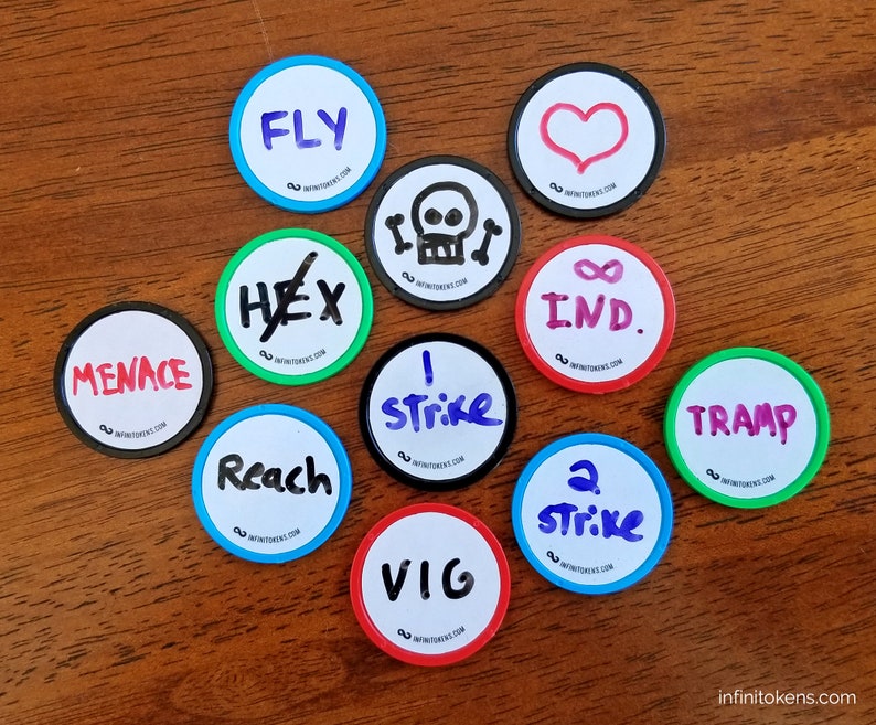 May include: Circular game tokens with handwritten text and symbols, such as "FLY," "MENACE," and a skull. Each token features a white centre, a coloured border, and the text "infinitetokens.com."