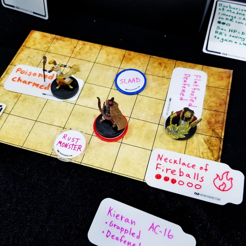May include: A tabletop role-playing game setup with miniature figures on a grid map. The scene includes character cards, status markers, and a "Necklace of Fireballs" card. The figures are on round bases, and the cards have handwritten text.