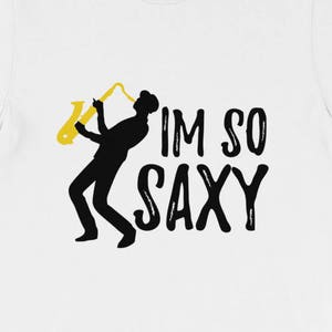 Puede incluir: Camiseta blanca con una silueta negra de una persona tocando el saxofón. El texto "I'm so saxy" está impreso en negro debajo de la silueta.