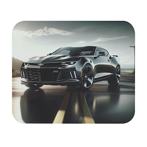May include: A black Chevrolet Camaro sports car is parked on a paved road with yellow lines. The car is facing the camera and has a black grille with a gold Chevrolet emblem.