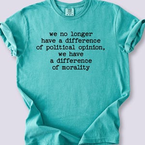 May include: A turquoise t-shirt with the text "we no longer have a difference of political opinion, we have a difference of morality" in black. The shirt is folded, with the sleeves rolled up.
