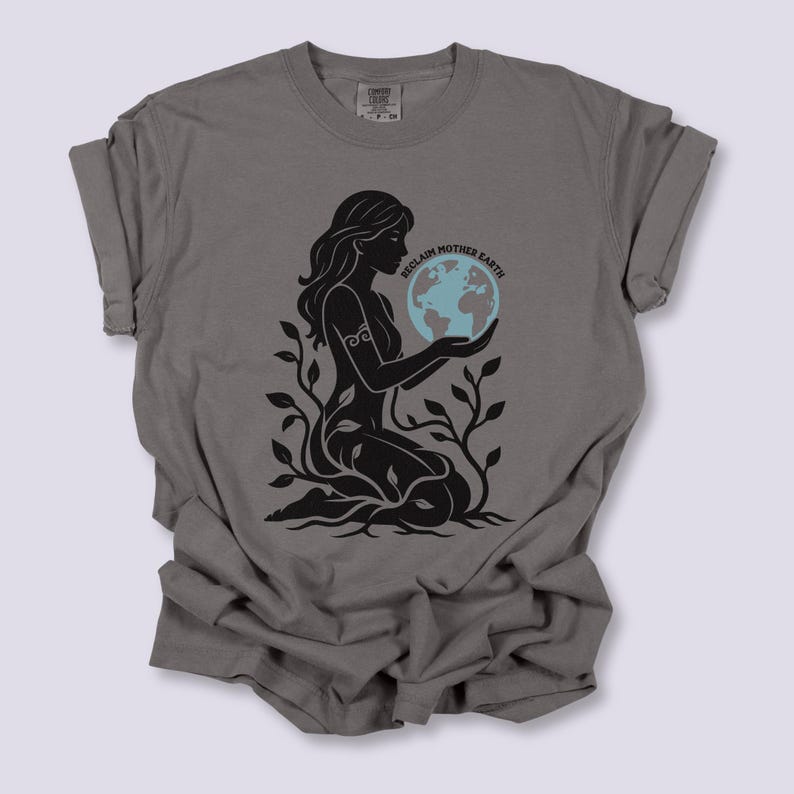 May include: Gray t-shirt featuring a black graphic of a woman holding a blue and green globe, surrounded by leaves. The text "RECLAIM MOTHER EARTH" is above the globe. The shirt is made of a soft material.
