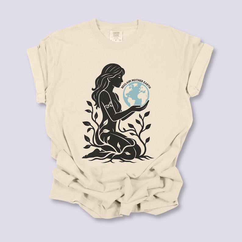 May include: Cream-colored t-shirt featuring a black silhouette of a woman holding a blue globe, with the text "RECLAIM MOTHER EARTH". The woman is surrounded by plant-like imagery.