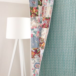 May include: A patchwork quilt with a floral pattern in shades of red, pink, blue, and green. The quilt is folded in half and has a light blue and white striped backing.