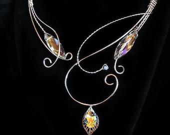 May include: A silver wire necklace with a teardrop-shaped crystal pendant and two smaller crystals on the sides. The necklace is on a black velvet background.