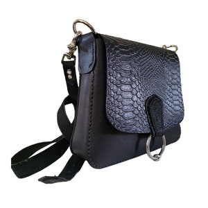 May include: A black leather crossbody bag with a snakeskin pattern flap. The bag has a silver ring detail and a long adjustable strap.