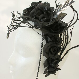May include: A black floral crown with black roses and branches, accented with a black chain and a single black feather.
