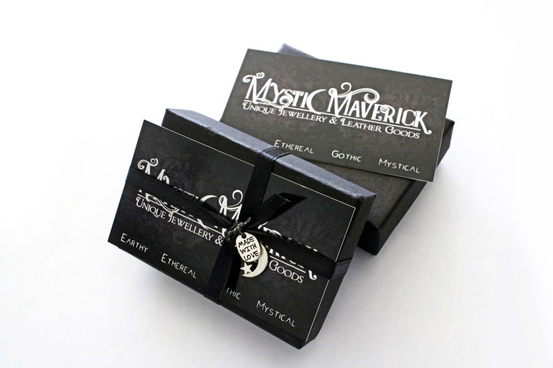 May include: Black boxes with the text "Mystic Maverick Unique Jewellery & Leather Goods" in white. The boxes are tied with a black ribbon and a charm that says "Made with Love". The boxes have the words "Earthy, Ethereal, Gothic, Mystical".