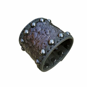 May include: A brown leather cuff bracelet with silver studs and an embossed floral design.