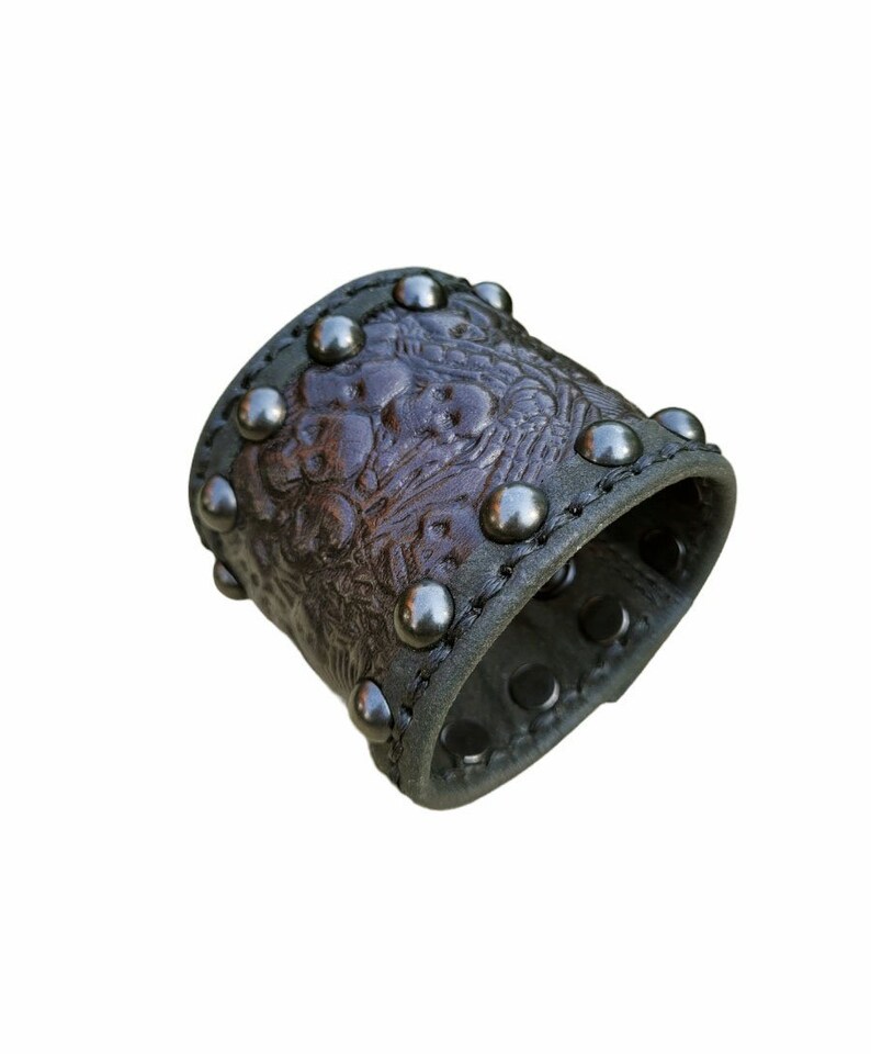 May include: A brown leather cuff bracelet with silver studs and an embossed floral design.