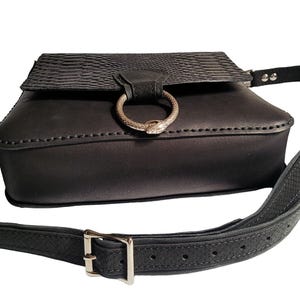 May include: Black leather crossbody bag with a snake-shaped ring detail and an adjustable strap.