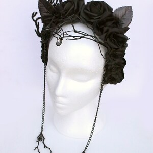 May include: A black floral crown with black roses and leaves, accented with a crystal and dangling chains with black crystal accents.