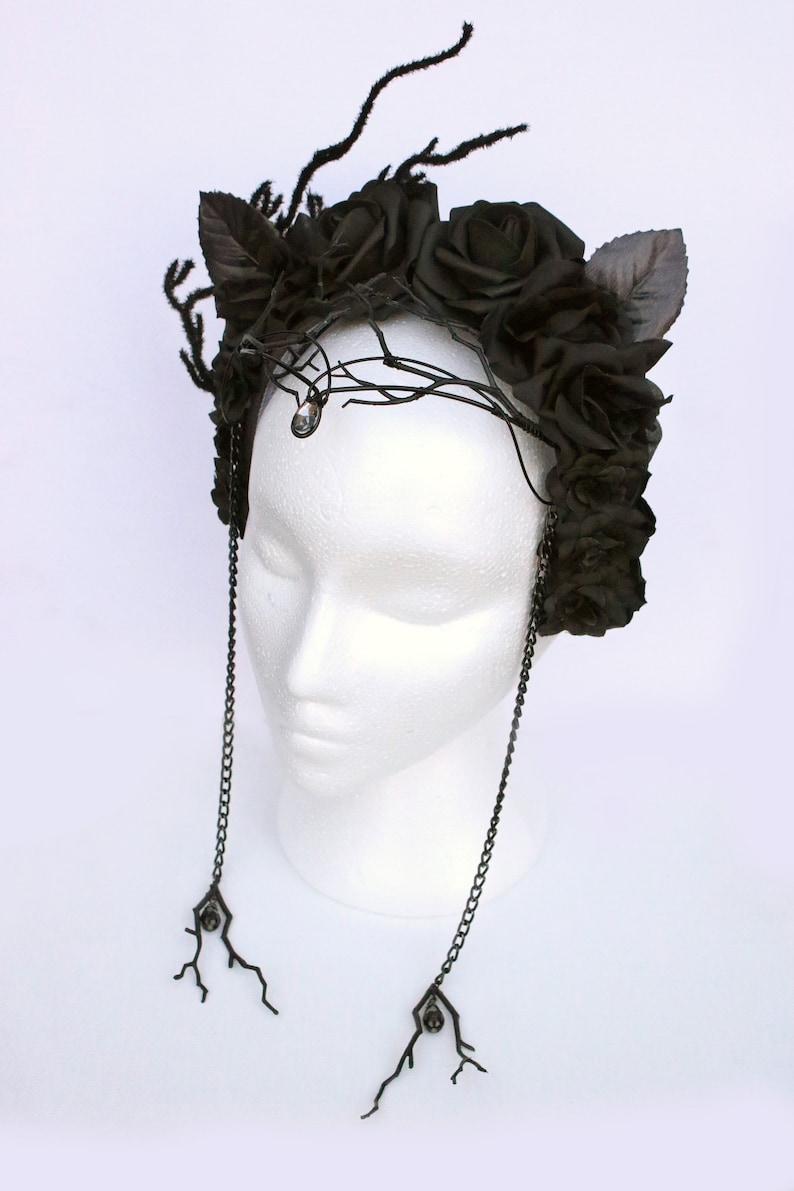 May include: A black floral crown with black roses and leaves, accented with a crystal and dangling chains with black crystal accents.