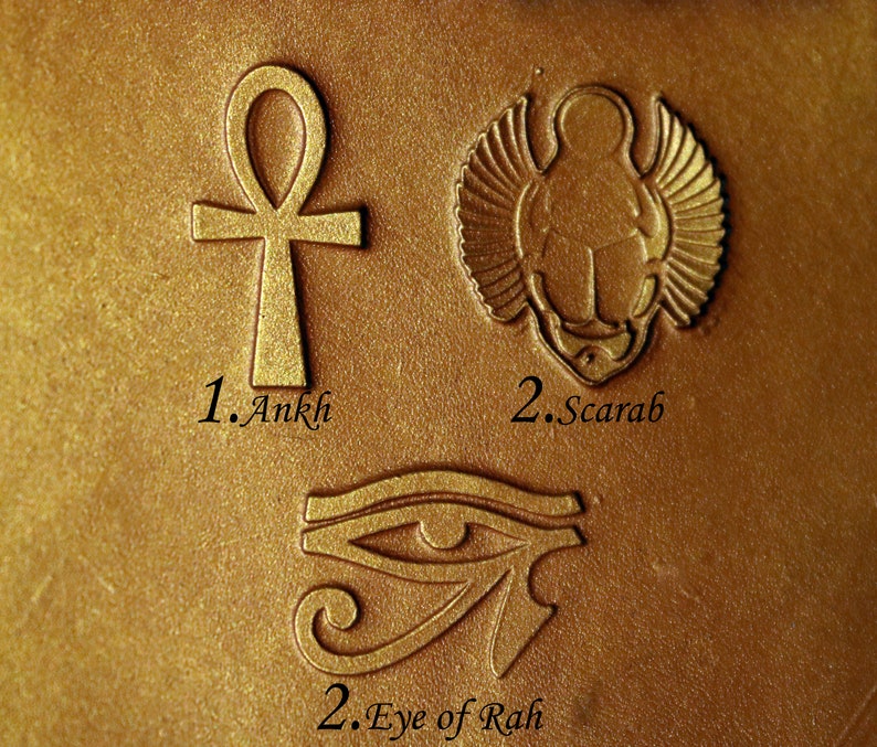 May include: Close-up of three gold-colored metal stamps with Egyptian symbols. The stamps are labeled "1. Ankh", "2. Scarab", and "2. Eye of Rah".
