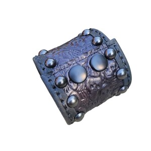 May include: A black leather cuff bracelet with silver studs and an embossed floral design.