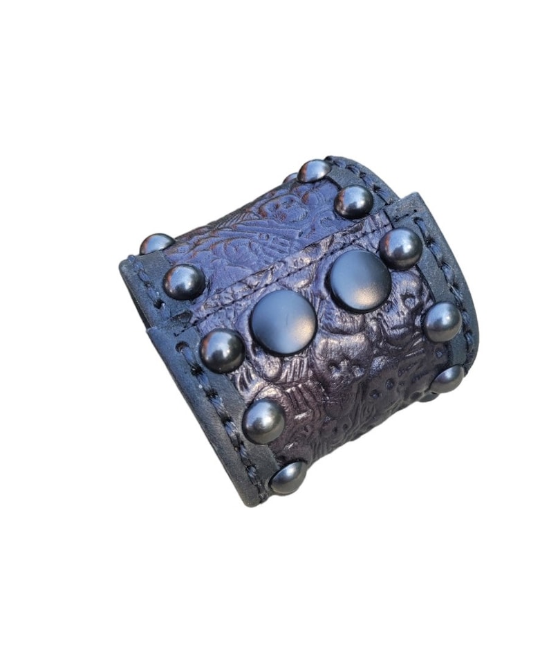 May include: A black leather cuff bracelet with silver studs and an embossed floral design.