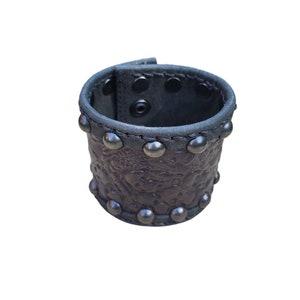 May include: A brown leather cuff bracelet with silver studs and an embossed floral design.