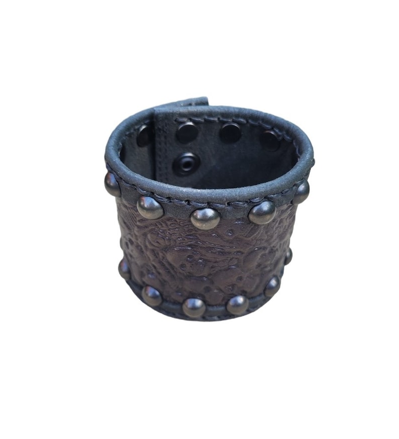 May include: A brown leather cuff bracelet with silver studs and an embossed floral design.