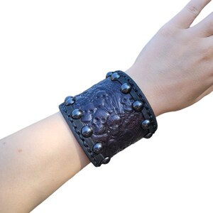 May include: A black leather cuff bracelet with a skull design and silver studs.