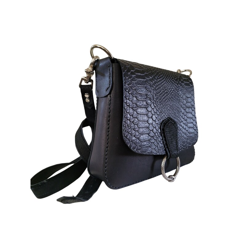 May include: A black leather crossbody bag with a snakeskin pattern flap. The bag has a silver ring detail and a long adjustable strap.