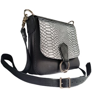 May include: A black leather crossbody bag with a silver snakeskin flap and a gold ring closure. The bag has a long adjustable strap.