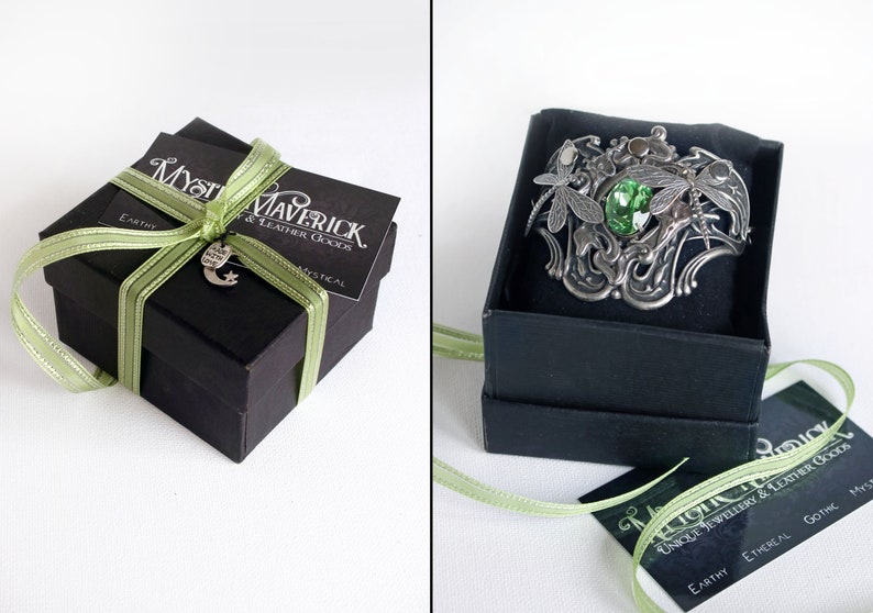 May include: A green gemstone ring with dragonfly accents, set in a silver band. The ring is displayed in a black gift box with a green ribbon and a tag that reads "Mystical Maverick & Leather Goods".