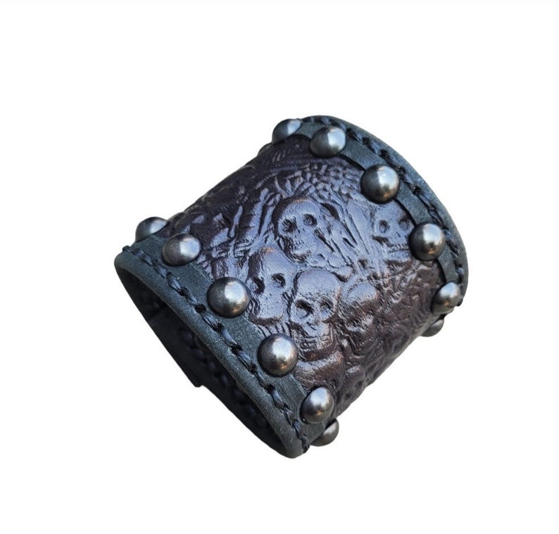 May include: A brown leather cuff bracelet with a skull design and silver studs.