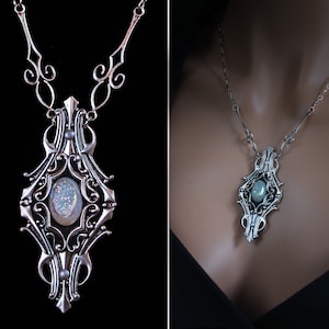 May include: Silver-toned pendant necklace with an ornate, Art Nouveau-inspired design. The pendant features a central oval-shaped stone with a sparkling, iridescent surface. The necklace has a delicate chain and decorative elements.