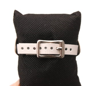 May include: A white leather watch strap with a silver buckle. The strap is on a black fabric display stand.