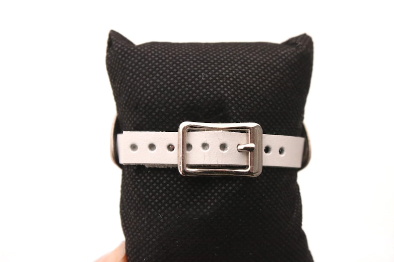 May include: A white leather watch strap with a silver buckle. The strap is on a black fabric display stand.