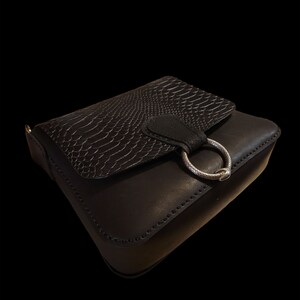May include: A black leather crossbody bag with a snakeskin pattern flap and a silver ring closure.