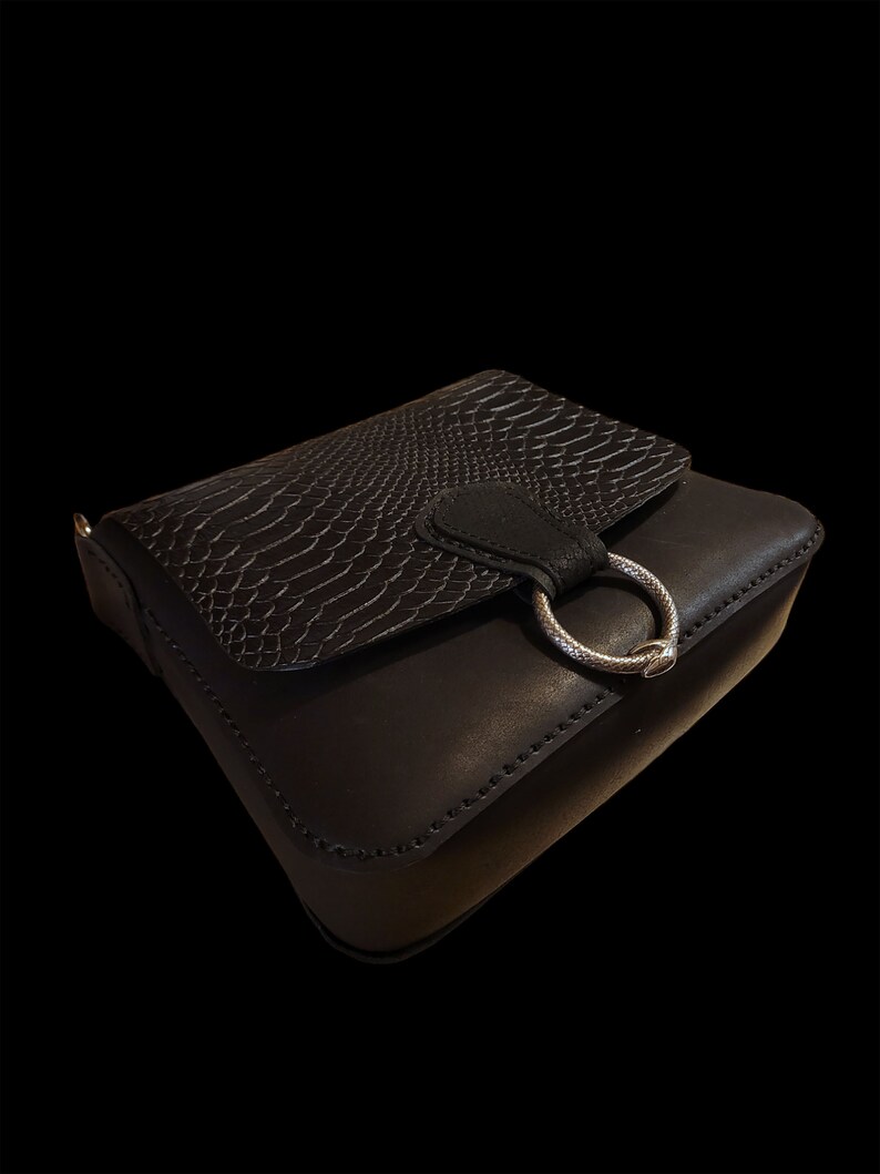 May include: A black leather crossbody bag with a snakeskin pattern flap and a silver ring closure.