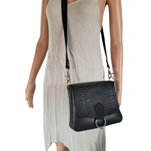 May include: A black leather crossbody bag with a snakeskin pattern and a silver ring detail.