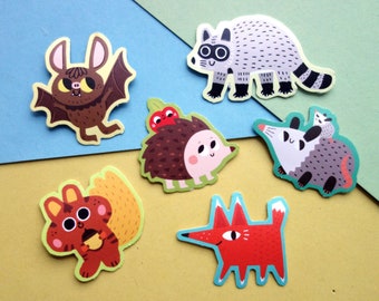May include: Six colourful animal stickers in a cartoon style. The stickers feature a bat, raccoon, hedgehog, opossum, squirrel and fox.