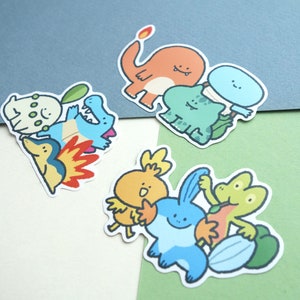 May include: A set of colourful cartoon character stickers featuring various Pokemon characters, including Charmander, Bulbasaur, Squirtle, and others. The stickers are printed on white paper and have a glossy finish.