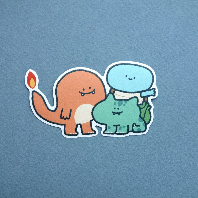 May include: A sticker featuring three cartoon characters: a red and orange fire-breathing dragon, a blue and white cloud-like creature, and a green frog-like creature.