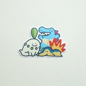 May include: A sticker featuring three cartoon Pokemon characters: a blue and white Squirtle, a green and white Bulbasaur, and a red and yellow Charmander.